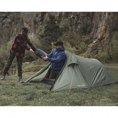 Reindal 2 tunneltent in een natuurlijke omgeving, twee personen dragen een slaapzak door de open ingang van de tent.
